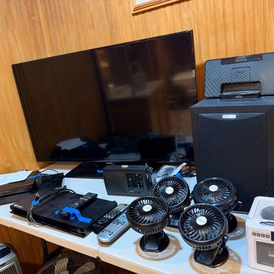 Sale Photo Thumbnail #100: Collection of home electronics, including a flat-screen television, a Polk Audio speaker system, a compact CD cassette player, small personal desk fans, and media players with remotes.