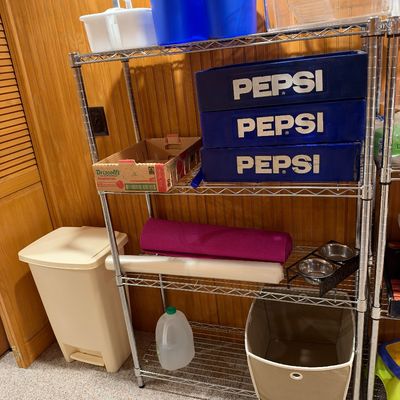 Sale Photo Thumbnail #119: Metal wire shelving unit holding various household items, including vintage blue Pepsi crates, cleaning caddies, a yoga mat, and a fabric storage bin.