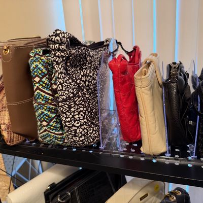 Sale Photo Thumbnail #24: Collection of women's handbags and purses, including leather and patterned fabric styles, neatly displayed on a shelf with clear dividers.