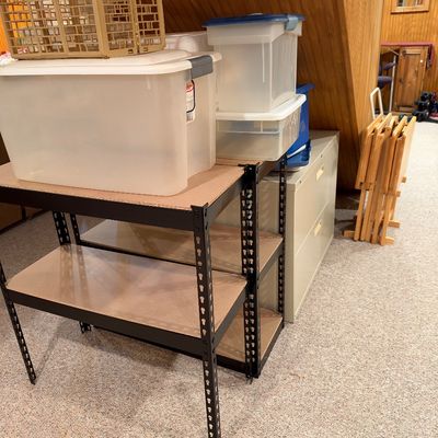 Sale Photo Thumbnail #20: Black metal heavy-duty shelving unit holding plastic storage totes, set alongside a two-drawer metal filing cabinet and wooden TV tray set.