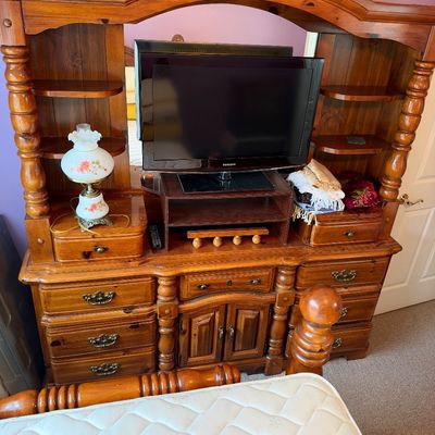 Sale Photo Thumbnail #53: Large rustic pine bedroom hutch dresser with attached mirror, turned columns, and multiple drawers, housing a small flat-screen television and a vintage floral accent lamp.
