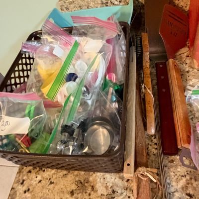 Sale Photo Thumbnail #78: Assorted kitchen items including small accessories bagged in a brown weave basket and grilling spatulas with long metal tongs alongside.