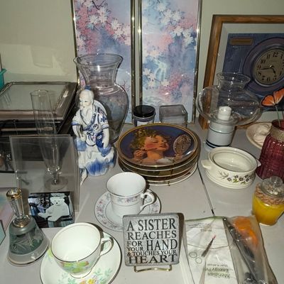 Sale Photo Thumbnail #73: Collection of tabletop home decor items, including floral framed art panels, fine china teacups, a porcelain wise man figurine, decor plates, and glass candleholders.