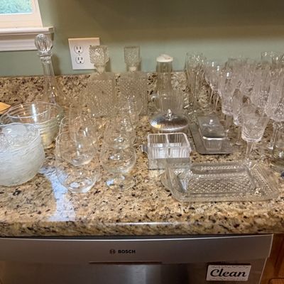 Sale Photo Thumbnail #89: Large collection of vintage glassware arranged on a granite countertop, including crystal decanters, stemware, snifters, bowls, and serving dishes.