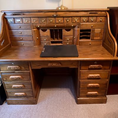 Sale Photo Thumbnail #43: Large wooden roll-top desk featuring multiple drawers and organizer cubbies, topped with a brass banker's lamp.