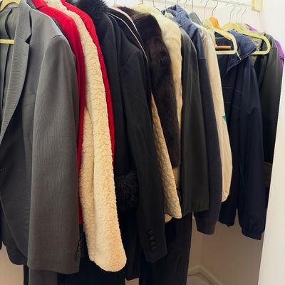 Sale Photo Thumbnail #60: Selection of men's and women's outerwear and blazers hanging in a closet, including a charcoal suit jacket, shearling-lined coat, and casual windbreakers.