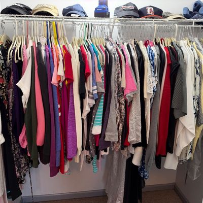 Sale Photo Thumbnail #56: A full closet of women's colorful clothing and tops hanging on a wire rack alongside several baseball caps on the top shelf.