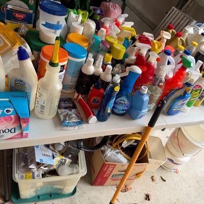 Sale Photo Thumbnail #19: Large assortment of household cleaning supplies, laundry detergents, and spray bottles arranged on a white folding table.