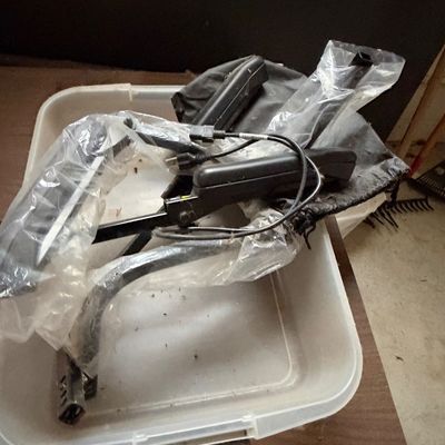 Sale Photo Thumbnail #6: Collection of black plastic wheelchair or mobility equipment attachments, including armrests and footrests, wrapped in protective plastic inside a clear storage tub.