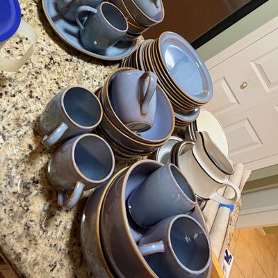 Sale Photo Thumbnail #84: Large collection of blue ceramic dinnerware featuring mugs, bowls, and plates with brown trim, displayed alongside a white stoneware cream pitcher.