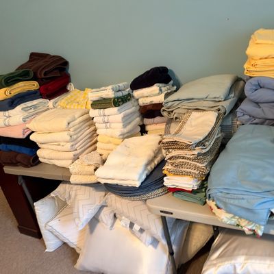 Sale Photo Thumbnail #30: Large collection of folded linens, towels, bedsheets, and pillows stacked on folding tables.