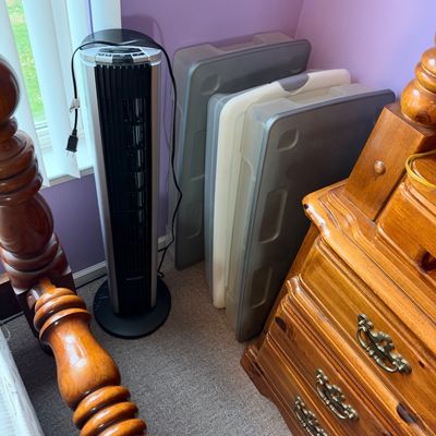 Sale Photo Thumbnail #52: Holmes modern oscillating tower fan in silver and black, standing beside several large plastic under-bed storage totes against a purple wall.