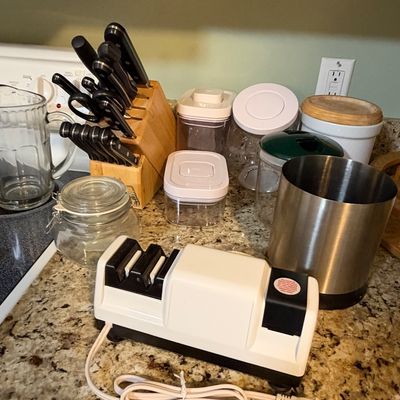 Sale Photo Thumbnail #87: Collection of kitchen items including a Chef'sChoice electric knife sharpener, a wooden knife block with knives, clear glass canisters, and plastic food storage containers.