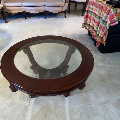 Round dark wood coffee table with an inset glass top, carved base, and beaded trim details.