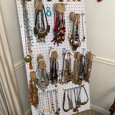 A pegboard display stand filled with an assortment of costume jewelry, including colorful beaded necklaces, statement bib pieces,...