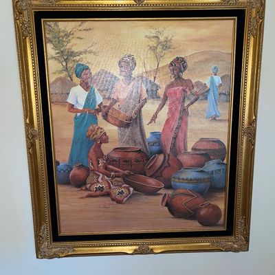 Framed canvas print depicting African women gathering with handcrafted pottery, set in an ornate gilded wood frame with a black velvet...