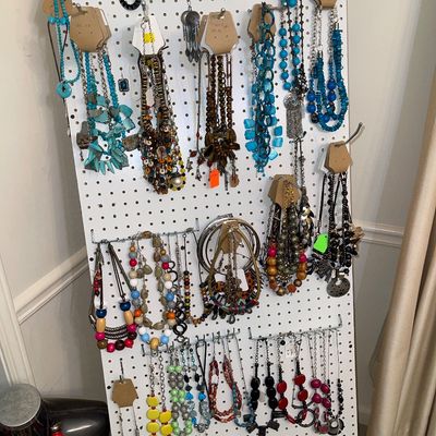 White pegboard display filled with an assortment of costume jewelry, including beaded necklaces, statement pendants, and earrings in...