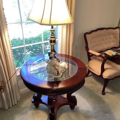 Traditional mahogany round side table with a glass inset top, featuring a brass table lamp and porcelain figurine.