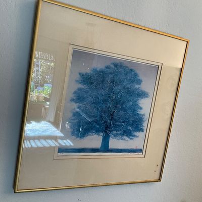 Sale Photo Thumbnail #142: Framed and matted artwork depicting a large blue tree, presented under glass in a slim gold-toned metal frame.