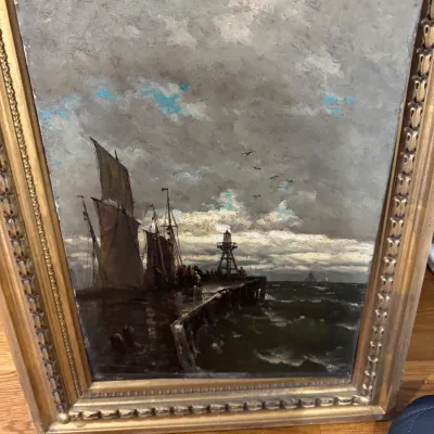 Framed oil painting depicting sailboat ships docked at a pier beside a beacon light under cloudy skies, housed in a decorative carved...