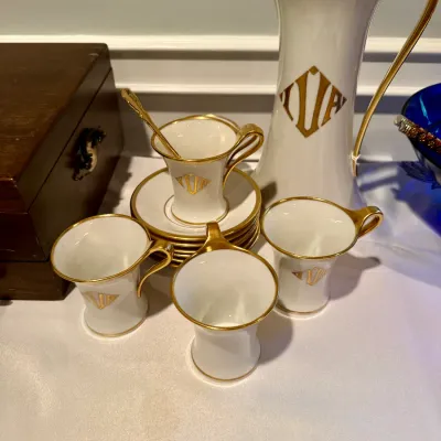 Vintage white porcelain coffee set featuring gold rims and monogrammed detailing, including a tall pot, four demitasse cups, and matching...