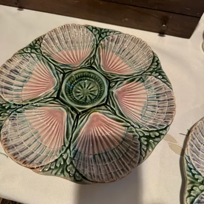 Vintage majolica oyster plate featuring six pink seashell-shaped wells with a central sauce well and a textured green rim.