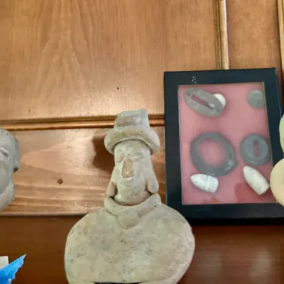 Collection of pre-Columbian style clay artifacts and figurines alongside a shadowbox displaying Civil War era bullets and relics.