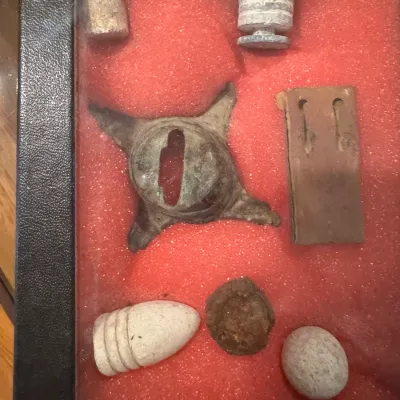 Framed shadow box display featuring excavated Civil War-era lead bullets, musket balls, and metallic relic fragments mounted on red felt.