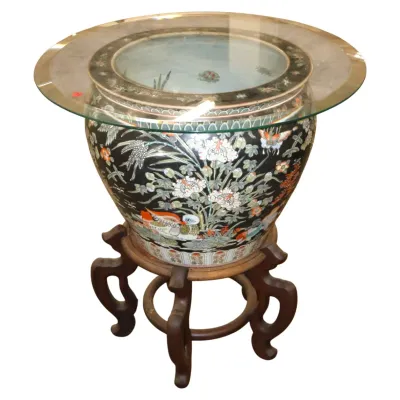 Sale Photo Thumbnail #264: Chinese polychrome porcelain fishbowl accent table, decorated with mandarin ducks, floral motifs, and butterflies, set on a carved dark wood stand with a round glass top.