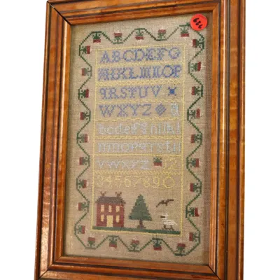 Sale Photo Thumbnail #133: Framed antique-style needlework alphabet sampler featuring a house, tree, and decorative border, set in a tiger maple wood frame.