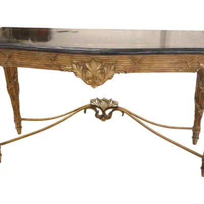 Sale Photo Thumbnail #28: Manner of Maitland Smith - French Neoclassical style gilded console table featuring a dark marble top, carved acanthus leaf detailing, fluted tapered legs, and a curved stretcher with a central finial motif.