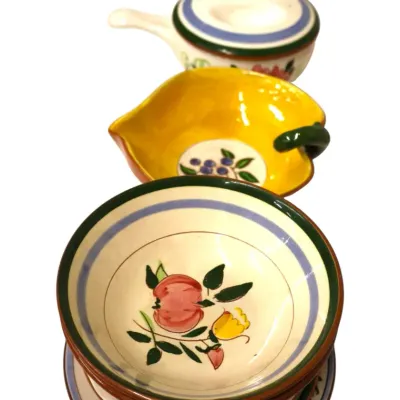 Sale Photo Thumbnail #288: Collection of hand-painted ceramic kitchenware, including a stack of fruit-patterned bowls, a leaf-shaped yellow dish, and covered ramekins with handles.