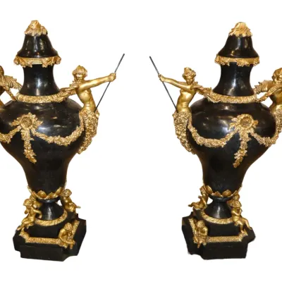 Sale Photo Thumbnail #15: Pair of ornate French Empire style black urns adorned with gilt bronze winged figures, floral garlands, and putti accents on square pedestals.