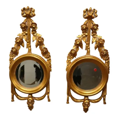 Sale Photo Thumbnail #142: Pair of vintage Neoclassical style gilded wall mirrors with ornate floral swag and bow crests surrounding circular frames.