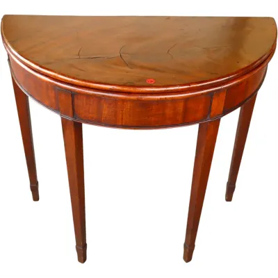 Sale Photo Thumbnail #236: Antique Hepplewhite-style mahogany demilune console table with tapered legs and string inlay detail, showing visible cracking on the top veneer.