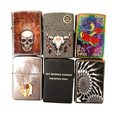 Sale Photo Thumbnail #146: Collection of six Zippo windproof pocket lighters featuring various graphic designs including skulls, a steer skull, a snake, and text.