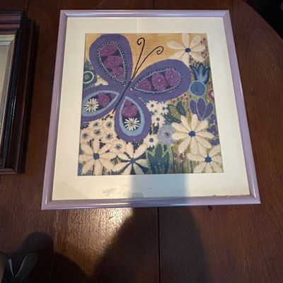 Sale Photo Thumbnail #67: Framed vintage embroidered textile artwork featuring a purple butterfly and white flowers in a matching lavender frame, circa 1970s.