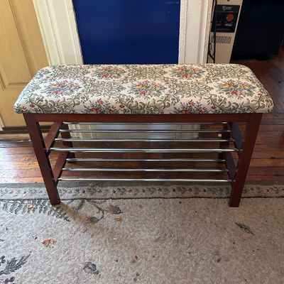 Sale Photo Thumbnail #103: Vintage shoe rack bench featuring a wooden frame with metal rungs and a cushioned top upholstered in a floral tapestry fabric.