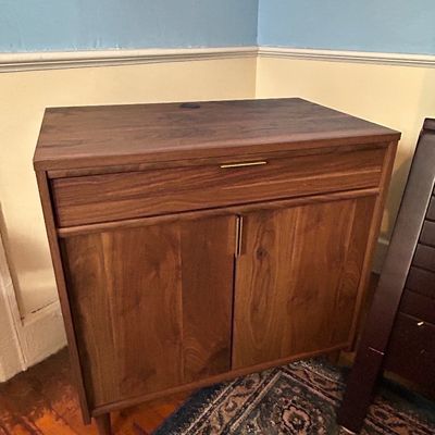 Sale Photo Thumbnail #91: Modern mid-century style walnut cabinet featuring a top pull-out tray drawer, double doors with slim brass hardware, and tapered wooden legs.