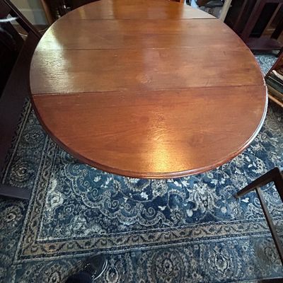Sale Photo Thumbnail #94: Round wooden drop-leaf dining table with a warm stain, resting on an ornate patterned area rug.