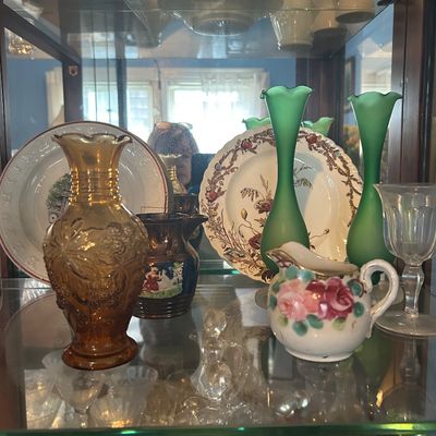 Sale Photo Thumbnail #59: Glass display cabinet shelf filled with vintage collectibles, including amber carnival glass, satin green swing vases, decorative china plates, and a hand-painted floral creamer.