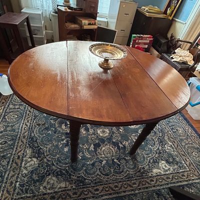Sale Photo Thumbnail #93: Round antique drop-leaf dining table in a warm wood finish, featuring turned legs and a decorative silver-plated centerpiece, set on a patterned area rug.