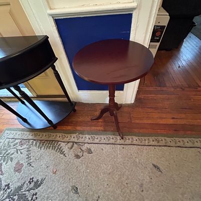 Sale Photo Thumbnail #100: Vintage mahogany pedestal accent table featuring a round top and a tripod cabriole base, shown beside a black demilune table.