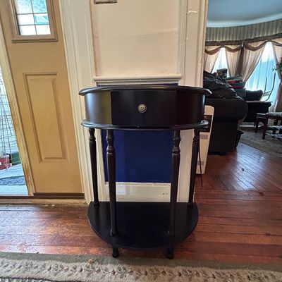 Sale Photo Thumbnail #101: Black painted half-round console table featuring turned legs, a single central drawer with a metallic knob, and a lower display shelf.