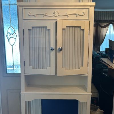 Sale Photo Thumbnail #50: White painted wooden hutch or cabinet featuring top scrollwork detail, dual doors with pleated fabric panels, and an open shelf below.
