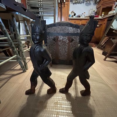 Sale Photo Thumbnail #118: Pair of antique Hessian soldier cast iron fireplace andirons with dark patina, positioned in front of an upholstered trunk.