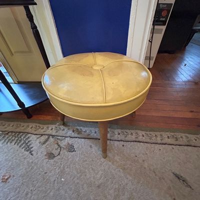 Sale Photo Thumbnail #99: Vintage mid-century round ottoman featuring button-tufted light yellow vinyl upholstery and tapered wooden legs, showing light wear.