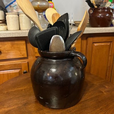 Sale Photo Thumbnail #16: Dark brown glazed ceramic bean pot filled with various wooden and plastic kitchen utensils.
