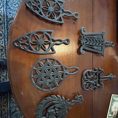 Sale Photo Thumbnail #36: Collection of six vintage cast iron sad iron trivets with various openwork designs, displayed on a wooden table top.