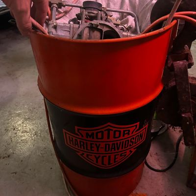 Sale Photo Thumbnail #103: Vintage orange and black Harley-Davidson oil drum container holding assorted automotive parts, showing age-appropriate wear.